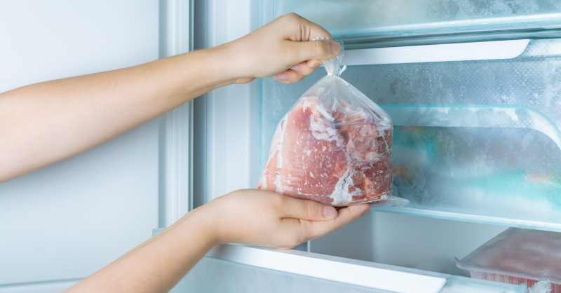 due mani che mettono a congelare la carne nel freezer di casa dentro un sacchetto di plastica